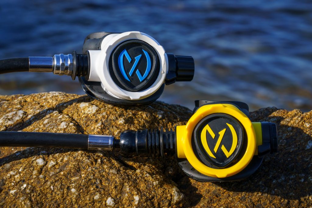 Two scuba diving regulators resting on a rock by the water.