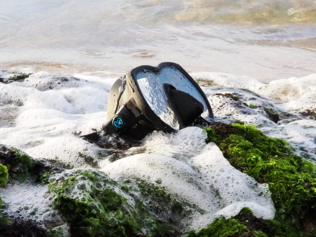 Snorkeling mask in foamy, green seaweed water.
